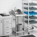 A Regency stainless steel filler table with a drop-in sink over a white cart.