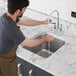 A person wearing a brown apron washing a Waterloo stainless steel sink.