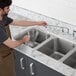 A man in an apron pouring water into a stainless steel sink.