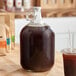 A clear Acopa growler filled with brown liquid on a table.