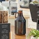 An Acopa amber glass growler with a cap on a counter.