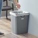A woman putting a plastic bag in a Lavex grey square trash can.