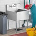A man in a blue uniform pouring water into a Regency stainless steel utility sink.