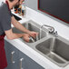 A man washing dishes in a Regency stainless steel drop-in sink with two compartments.
