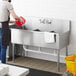A man pouring water into a Regency stainless steel utility sink.