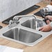A person washing a glass in a Regency stainless steel two compartment drop-in sink.
