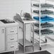 A Regency stainless steel filler table with a sink under it and a rack of dishes on top.