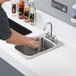 A person washing their hands in a Regency drop-in sink over bottles of liquid.