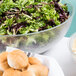 A bowl of salad and rolls next to a bowl of bread on a table.