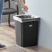 A person cleaning a Lavex black square trash can with a white towel.