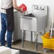 A man wearing a black apron pouring water into a Regency commercial utility sink.