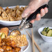 A hand holding a Carlisle black metal scoop over a plate of food.