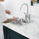 A person washing dishes in a Waterloo stainless steel drop-in sink.