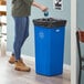 A woman in a corporate office cafeteria standing next to a Lavex blue square recycle bin with a white recycle symbol on top putting a bottle in it.