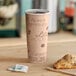 A close-up of a Choice Cafe Print paper hot cup filled with coffee on a table with a pastry.