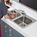A man washing dishes in a Regency stainless steel drop-in sink with two compartments.