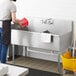 A man washing a Regency stainless steel utility sink on a counter.