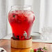 An Acopa glass beverage dispenser with red liquid in it on a wood table.