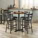 A Lancaster Table & Seating butcher block bar table with black chairs around it.