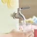 A hand filling a glass with water using an Acopa stainless steel spigot.