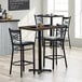 A Lancaster Table & Seating bar height butcher block table with two black chairs with cushions.