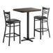 A bar height table set with a rectangular wood butcher block top and two black cross back chairs with cushioned seats.