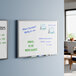 A wall-mounted 24 by 18 inch melamine whiteboard with an aluminum frame, shown with dry erase markers and notes written on it.