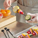 A person holding a skewer of yellow squash, peppers, and other vegetables on a tray.