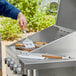 A person using Outset stainless steel tongs and spatula to cook food on a grill.