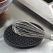 A wire whisk on a black Valor silicone trivet.