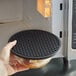 A hand using a Valor black silicone trivet under a bowl of food.