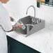 A person washing dishes in a Waterloo stainless steel drop-in sink with side splashes.