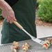 A person using an Outset stainless steel slotted turner to cook food on a grill.