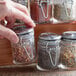 A hand holding a Tablecraft glass condiment jar filled with crushed red peppers.