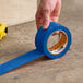 A roll of blue Shurtape VP 410 line set tape being applied to a concrete floor.