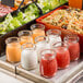 A Tablecraft glass jar filled with orange liquid on a table with a group of jars of different colored sauces and pasta salads.