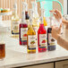 A clear acrylic three-tier organizer holding various flavored syrup bottles with pumps.