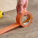 A roll of Shurtape VP 410 orange line set tape being applied to a concrete surface.