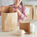 A woman opening a Sabert white food container from a brown paper bag.