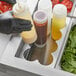 A person in black gloves using a Tablecraft stainless steel squeeze bottle holder to pour red liquid into a salad.