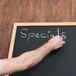 A person writing specials on an Aarco oak-framed black chalkboard.