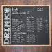 An Aarco oak-framed chalkboard menu with white writing on it.