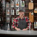 A man in a hat and apron behind a Tablecraft clear acrylic countertop safety shield.