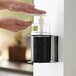 A person using a Steril-Sil black refillable hand soap dispenser to disinfect hands.