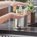 A person using a Steril-Sil stainless steel hand sanitizer dispenser on a counter.