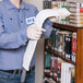 A man wearing blue gloves using a Unger ProFlex duster on a bookshelf.