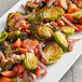 A plate of brussels sprouts and carrots with a pile of carrots on a table with a blurry carrot.