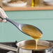A person using a Tablecraft solid silicone spoon to pour liquid onto a pan.