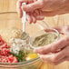 A person adding Regal Ground Marjoram to a bowl of meat.