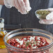 A person pouring Regal Mexican Oregano leaves into a bowl of red beans.